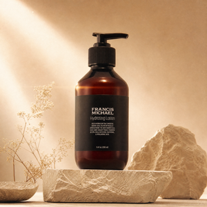 Brown bottle of Francis Michael Hydrating Lotion with black pump labeled 'Francis Michael' on a stone surface with a warm background