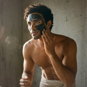 Man applying black facial mask, Francis Michael Detoxifying Mask, to his face against a neutral background