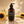 A bottle of Francis Michael Hydrating Lotion stands on a reflective surface with a white cream swirl around it, surrounded by sunflowers and leaf shadows in warm natural light.