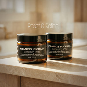 Two jars of Francis Michael skincare products, Francis Michael Exfoliating Paste and Francis Michael Detoxifying Mask, on a wooden surface with a blurred background.