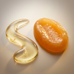 Yellow gel-like substance in a curved shape of Francis Michael Revitalizing Oil next to a round, orange-colored Francis Michael Nourishing Serum on a neutral background