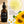 Francis Michael Cleansing Oil in an amber glass dropper bottle, shown next to a large yellow oil droplet, white daisies, sunflowers, and text describing its benefits on a warm beige background.