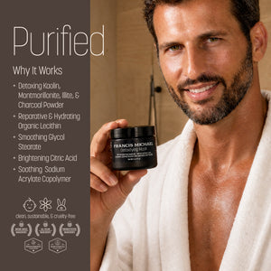 A man in a white robe holds a black jar of the Francis Michael Detoxifying Mask against a warm bathroom background, with a text panel on the left detailing the product's benefits.